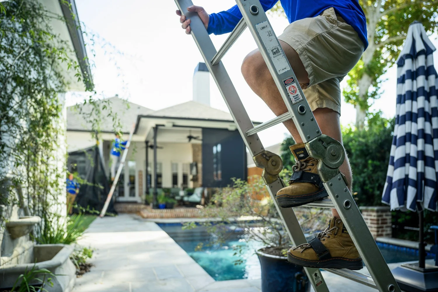 Epic Roofing crew member climbing a ladder beside a backyard pool