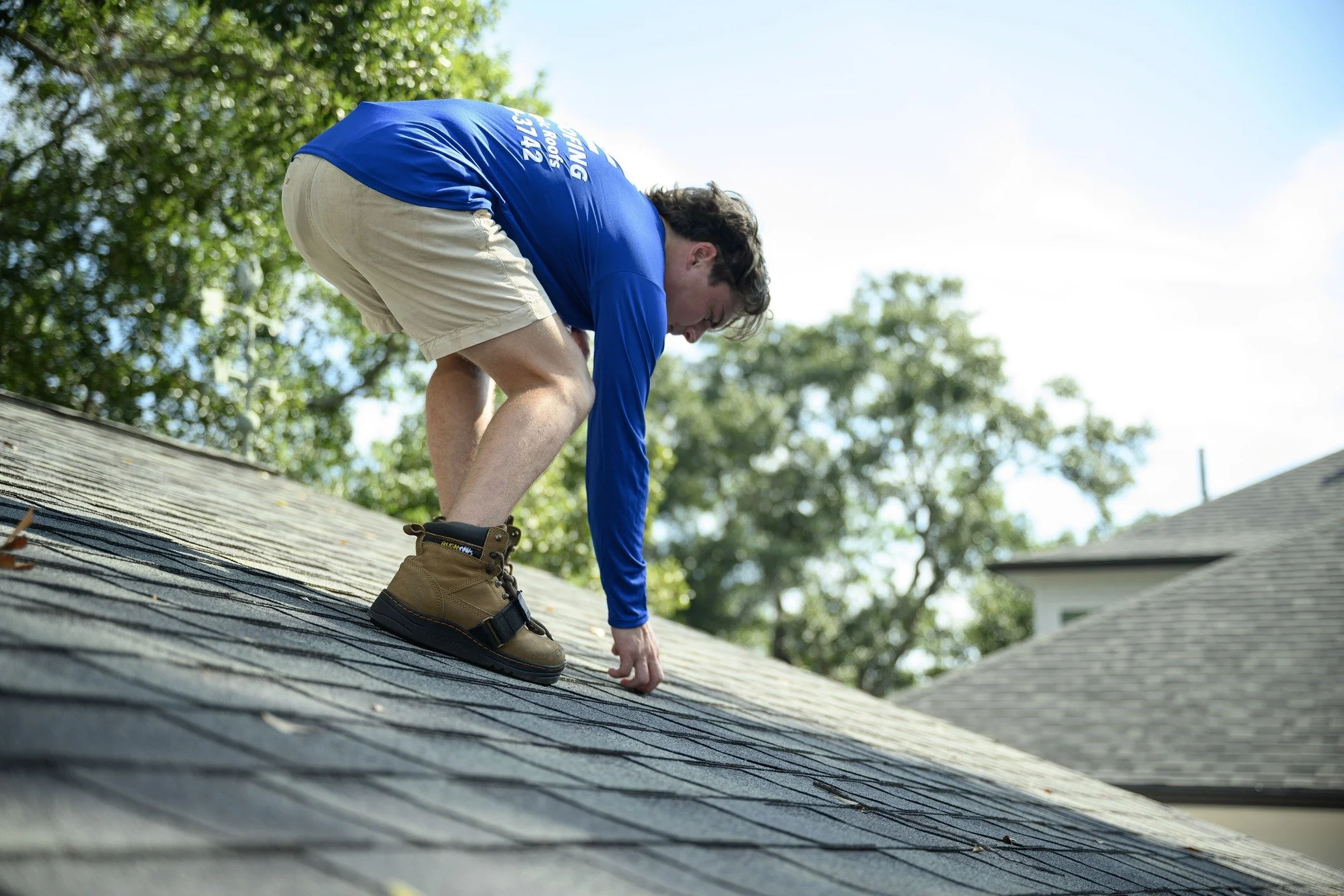Epic Roofing crew member bending over a grey shingle roof on a sunny day