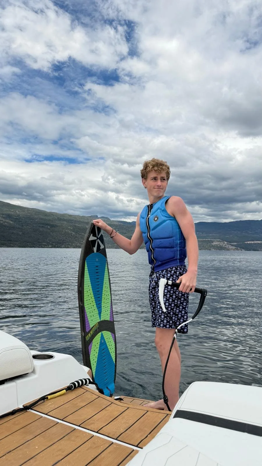 Charlie wearing a blue life jacket and holding a wakesurf board on a boat