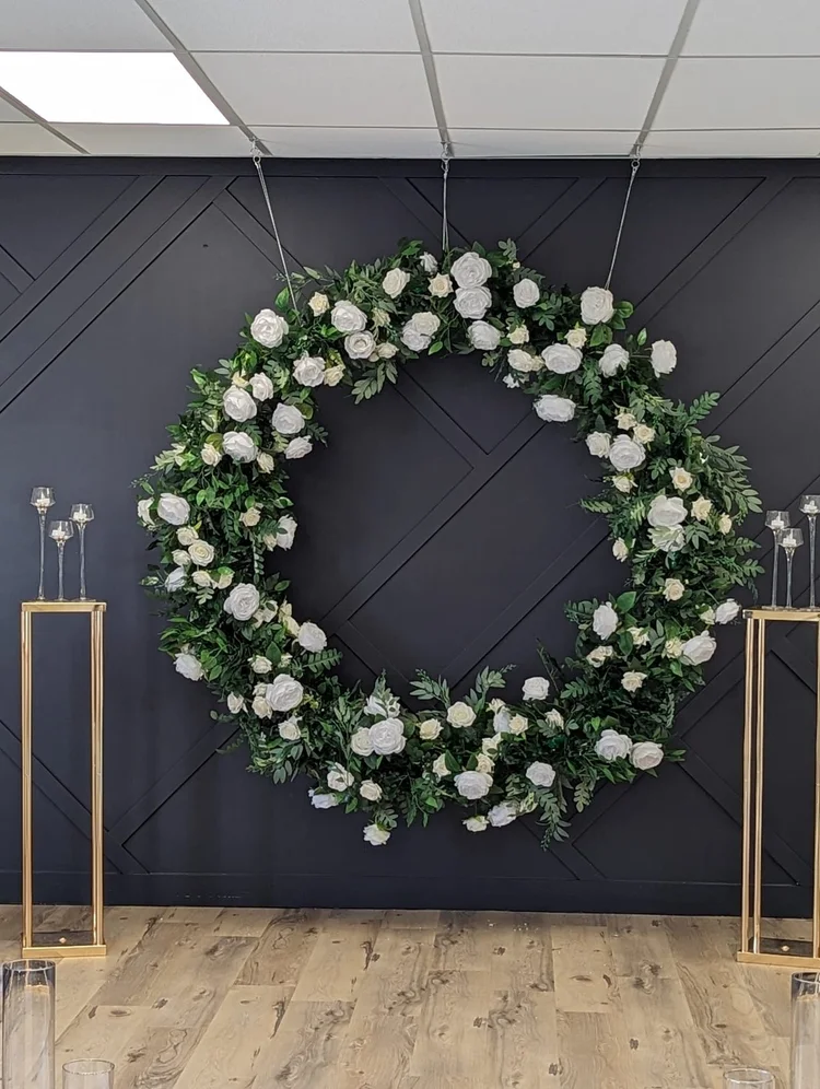 Large white rose and greenery floral wreath on a gold stand