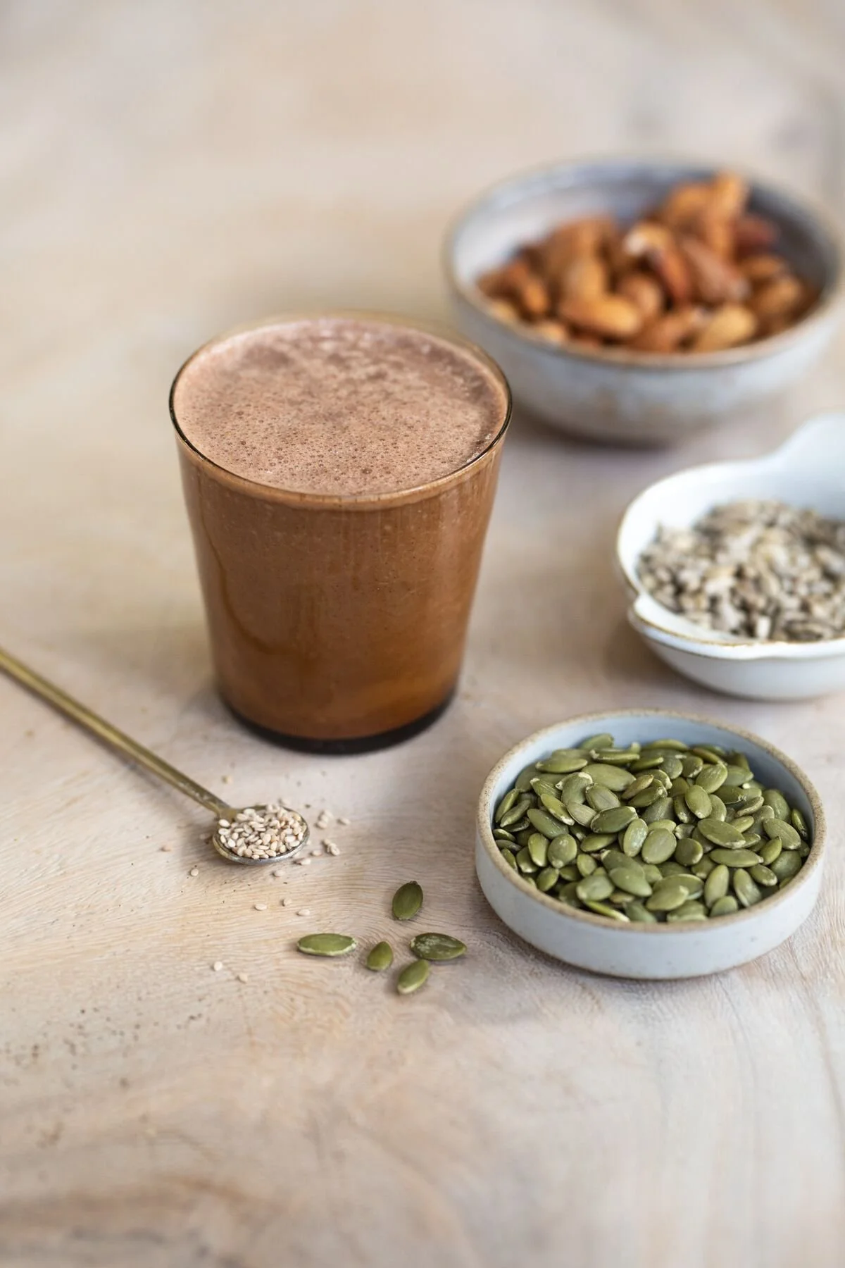 A spiced cacao drink beside bowls of nuts and seeds