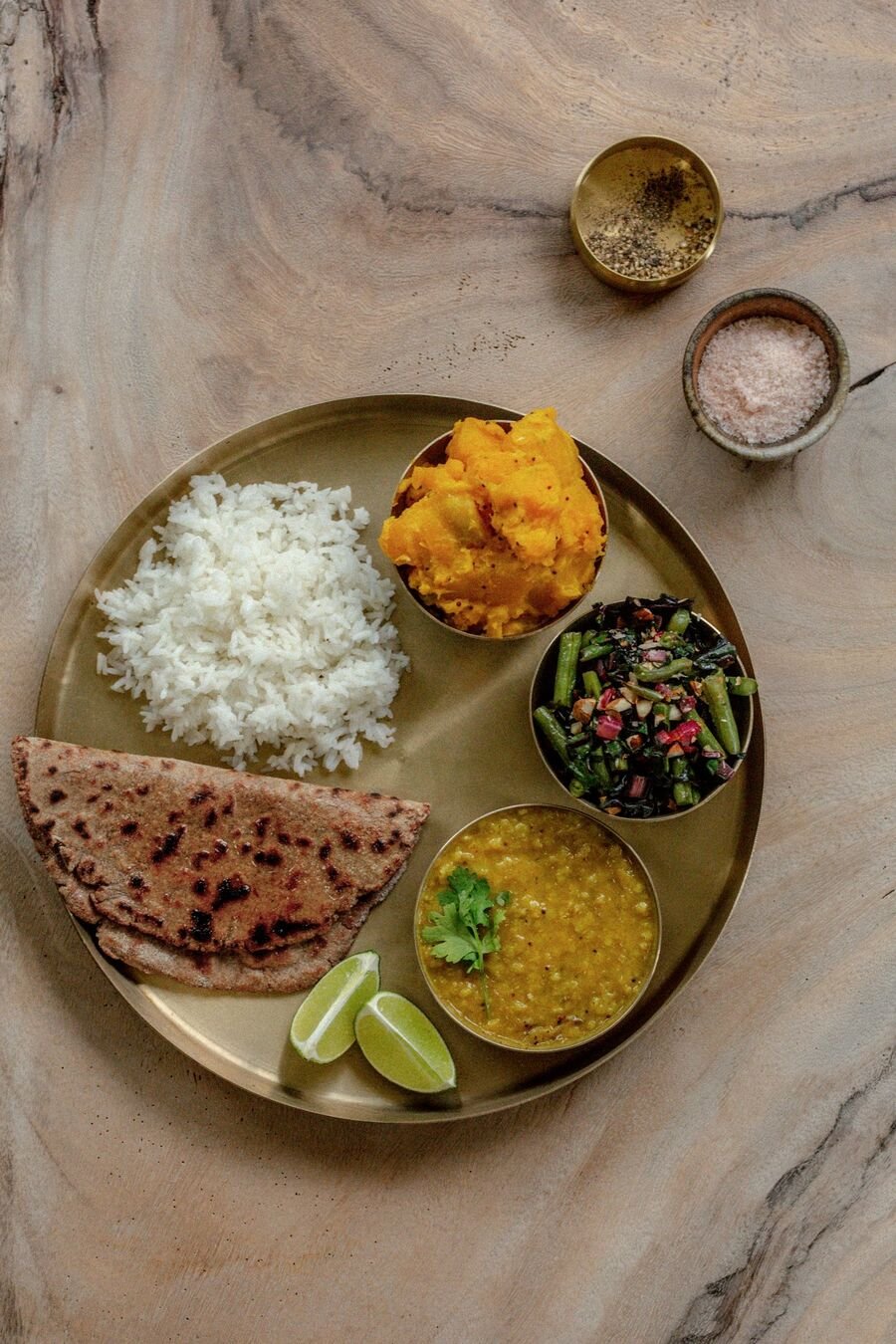 A brass thali with rice, flatbread, dal, roasted squash and greens