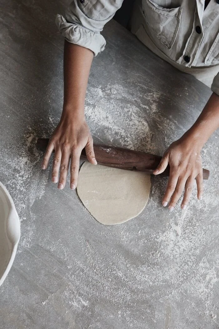 Hands rolling out flatbread dough with a wooden rolling pin