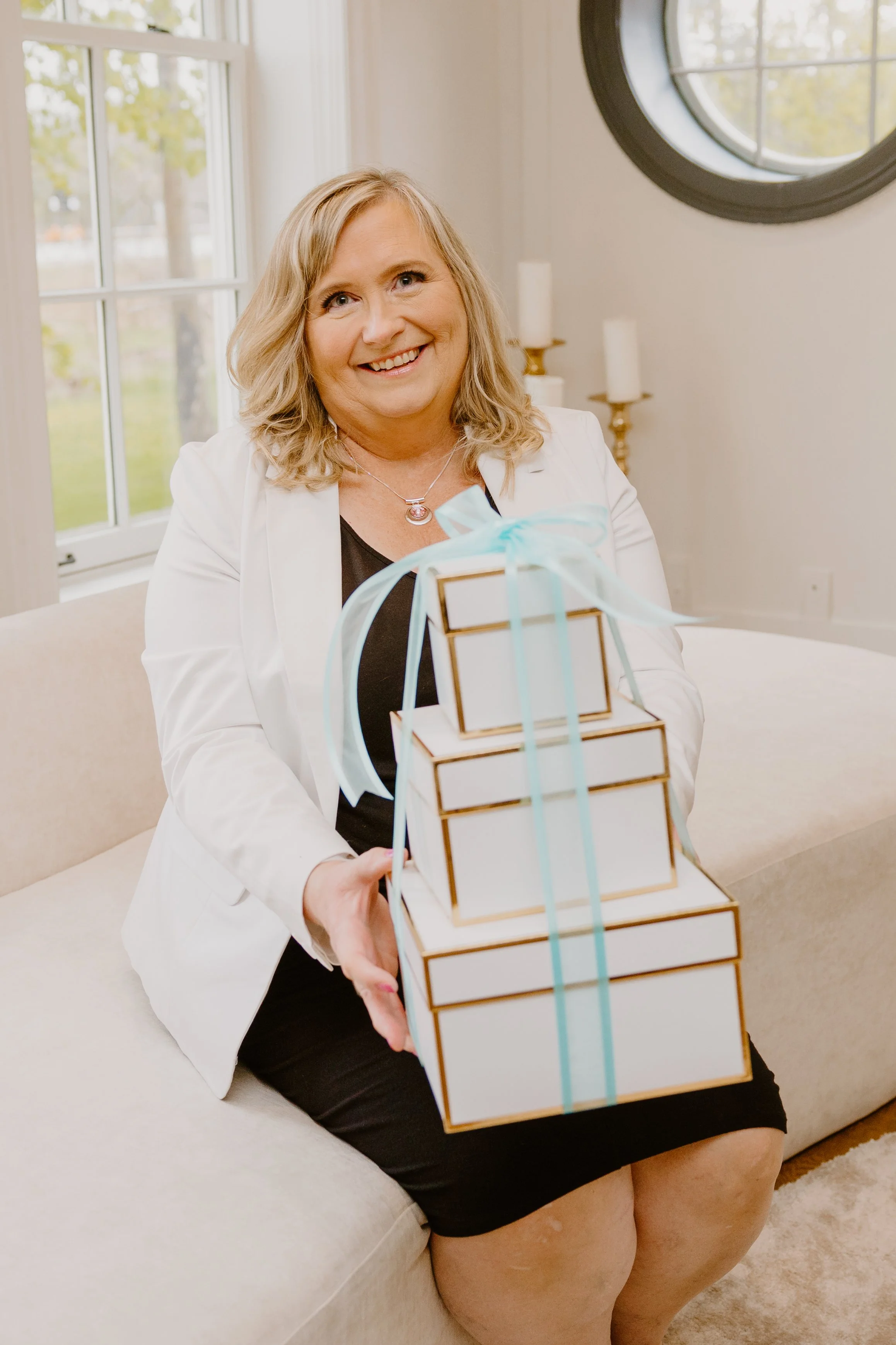 Judy of Wrapping Happy holding an elegant tower of wrapped gift boxes tied with teal ribbon