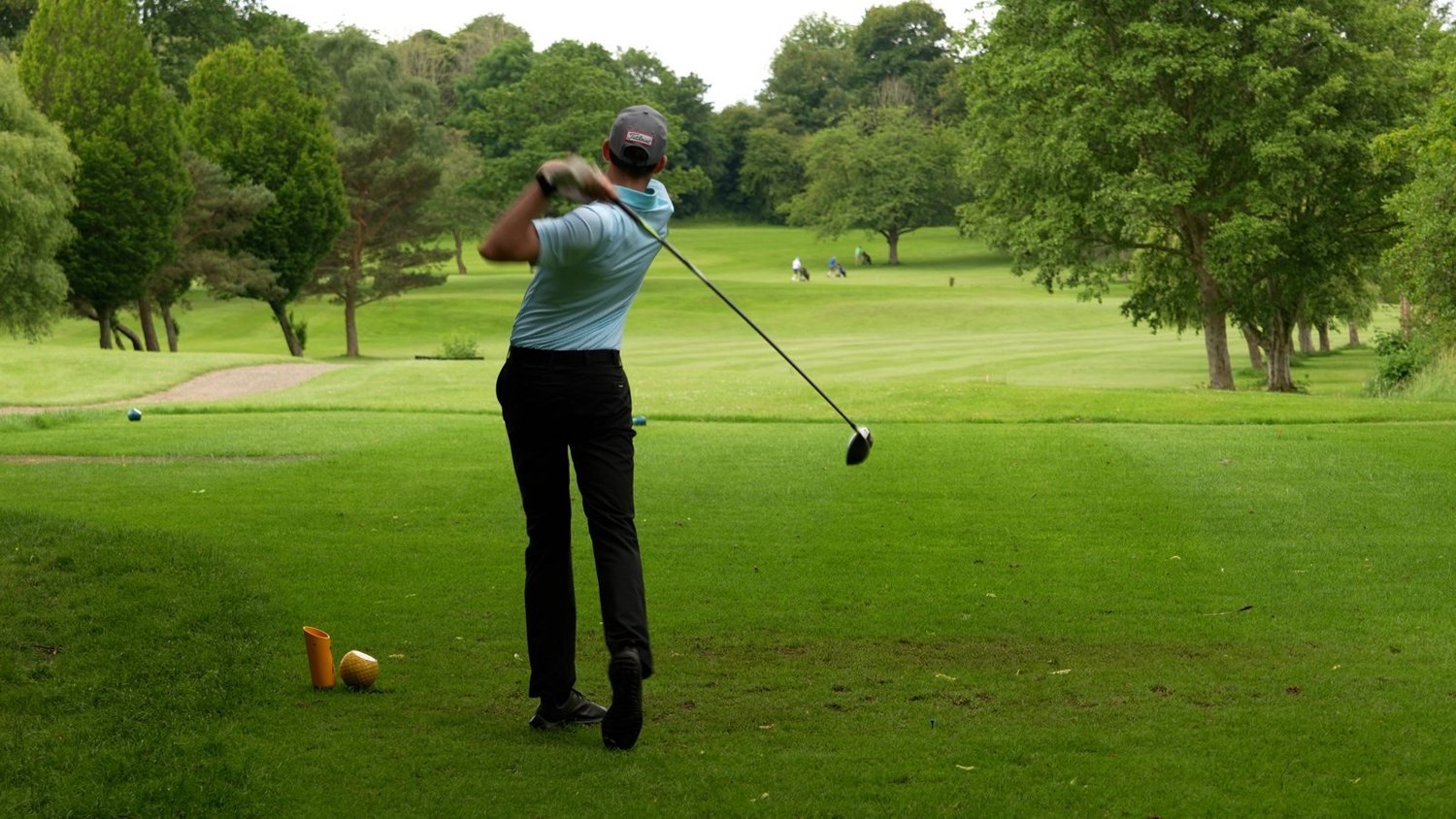 A golfer teeing off down a tree-lined fairway at Bedale