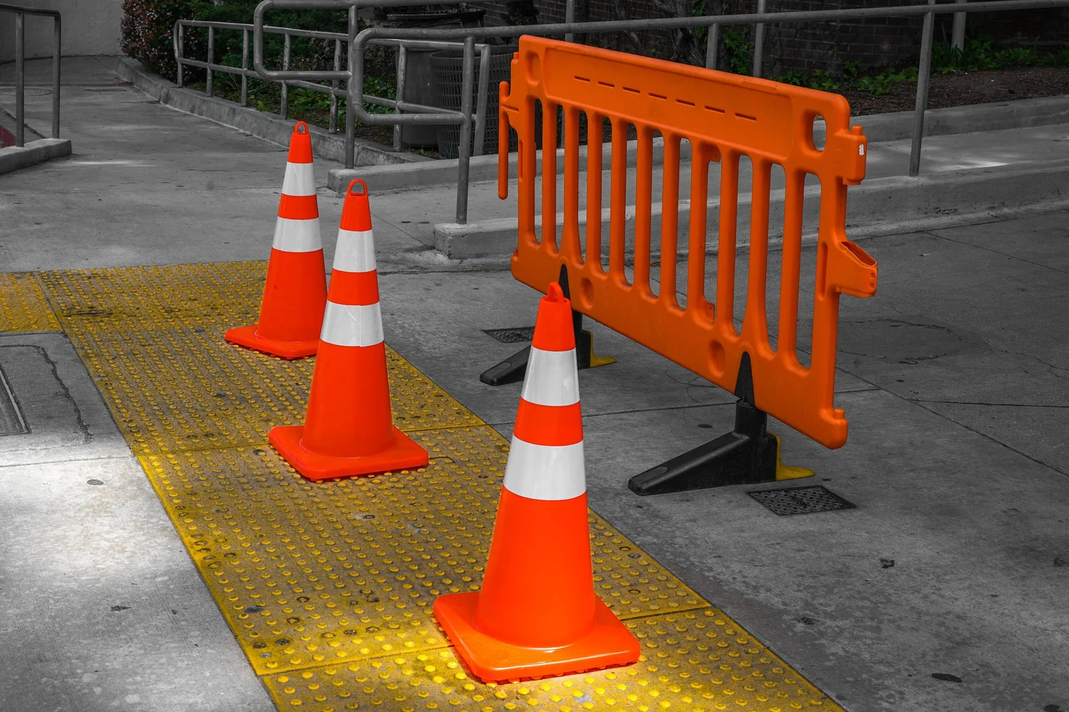 Orange traffic cones and a plastic barricade set up on a sidewalk