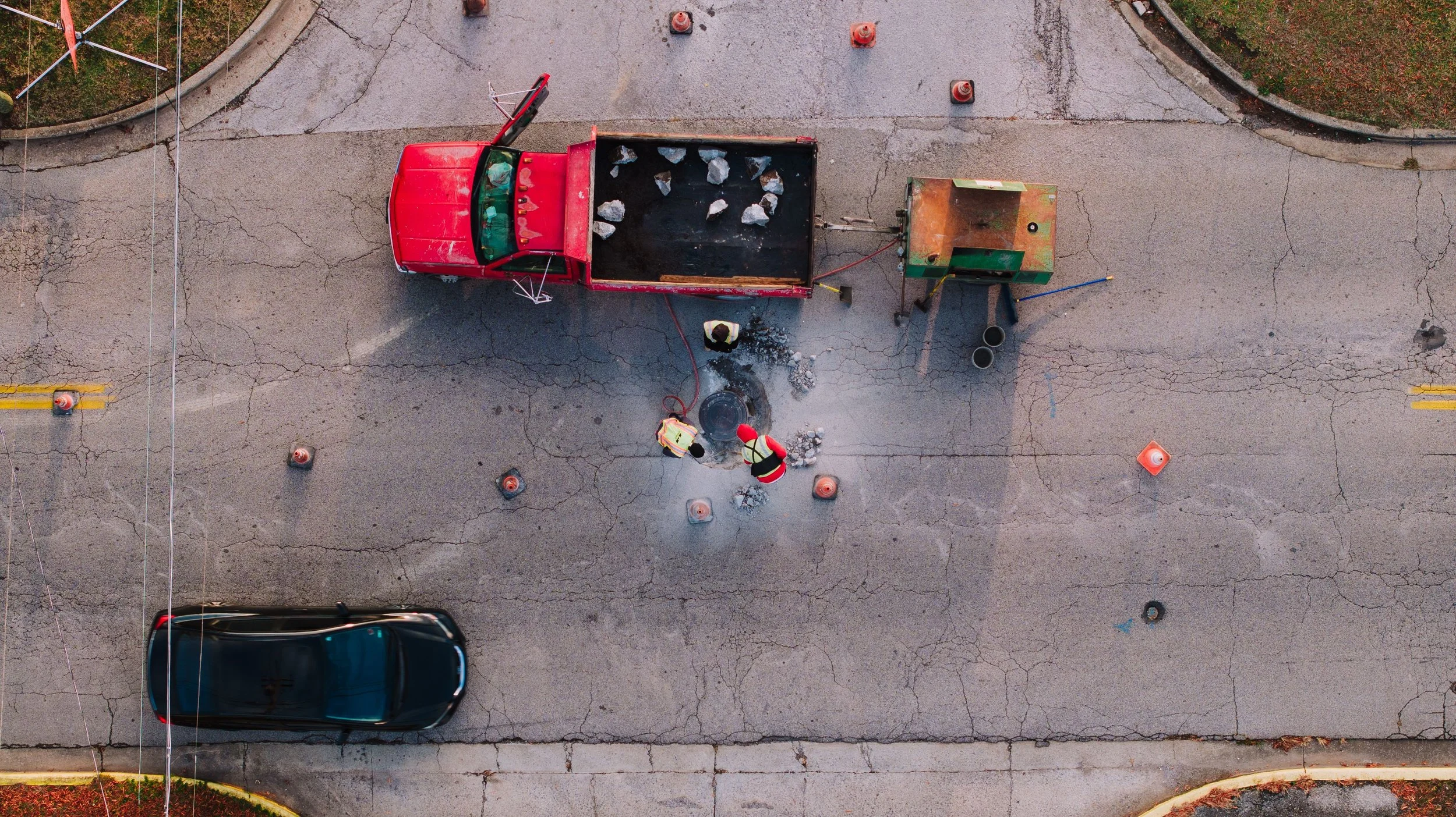 Overhead view of a road crew patching a street, surrounded by traffic cones