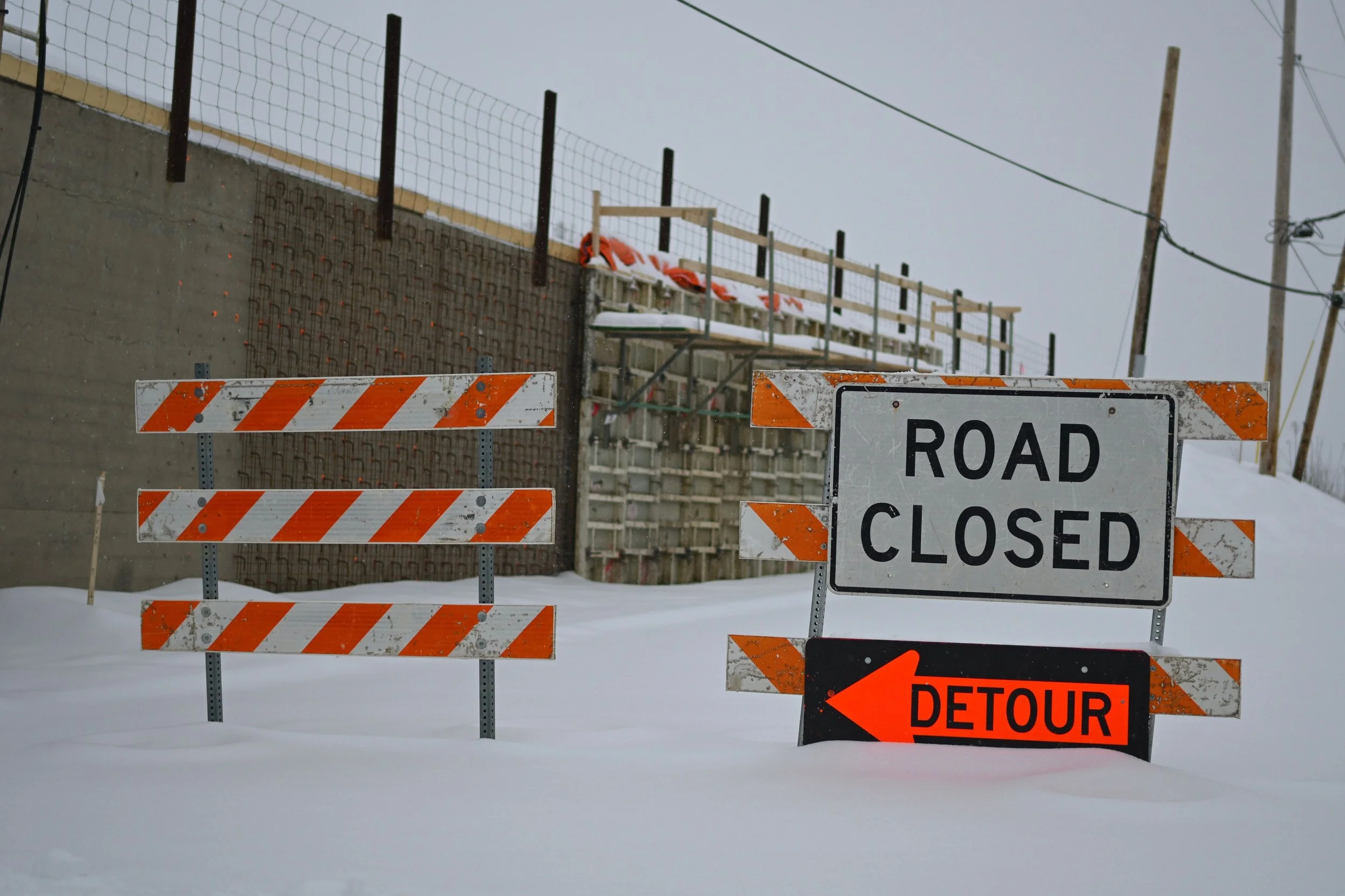 Road closed sign and detour arrow on snow-covered barricades