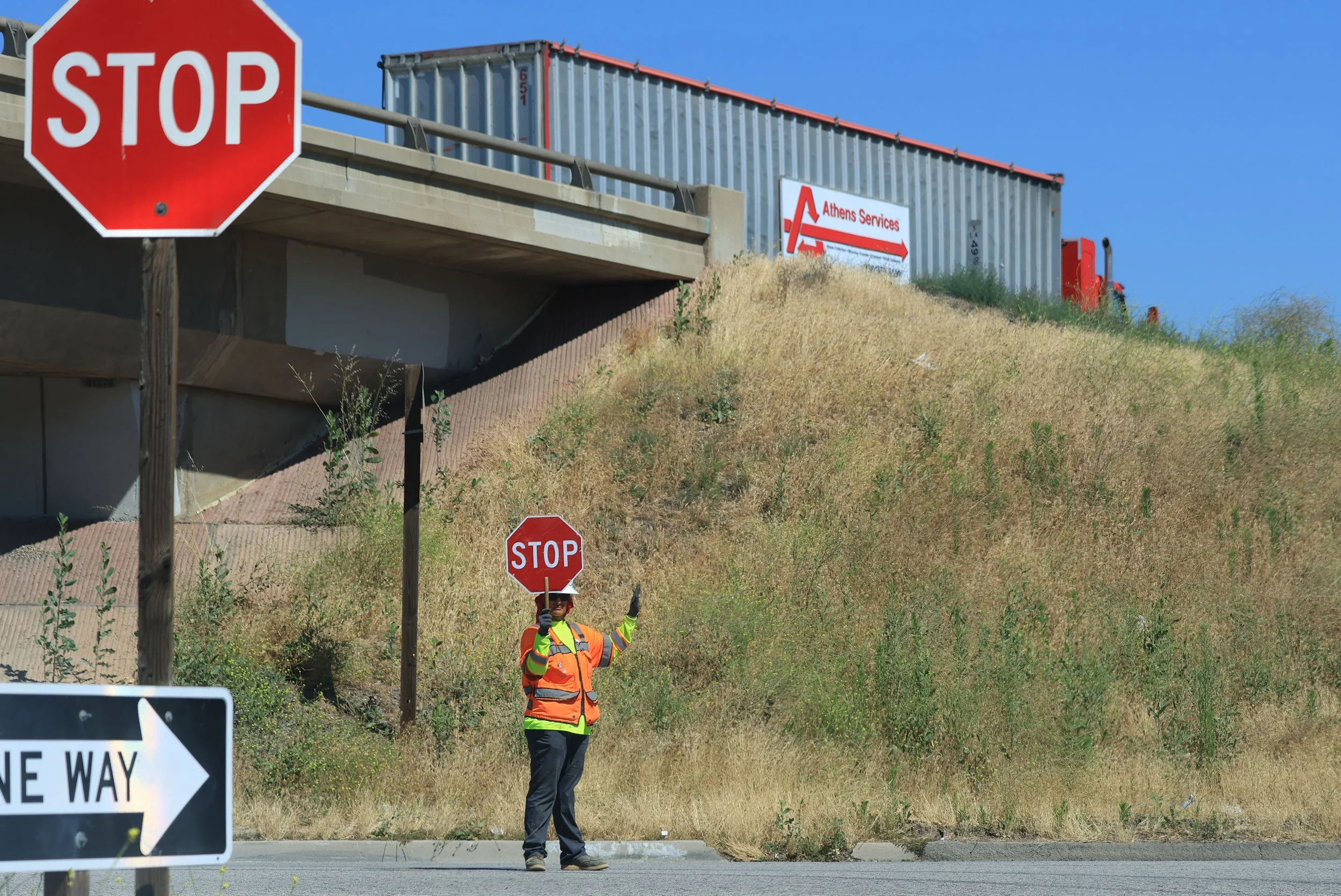 Flagger in high-visibility gear holding a STOP paddle beside a roadway