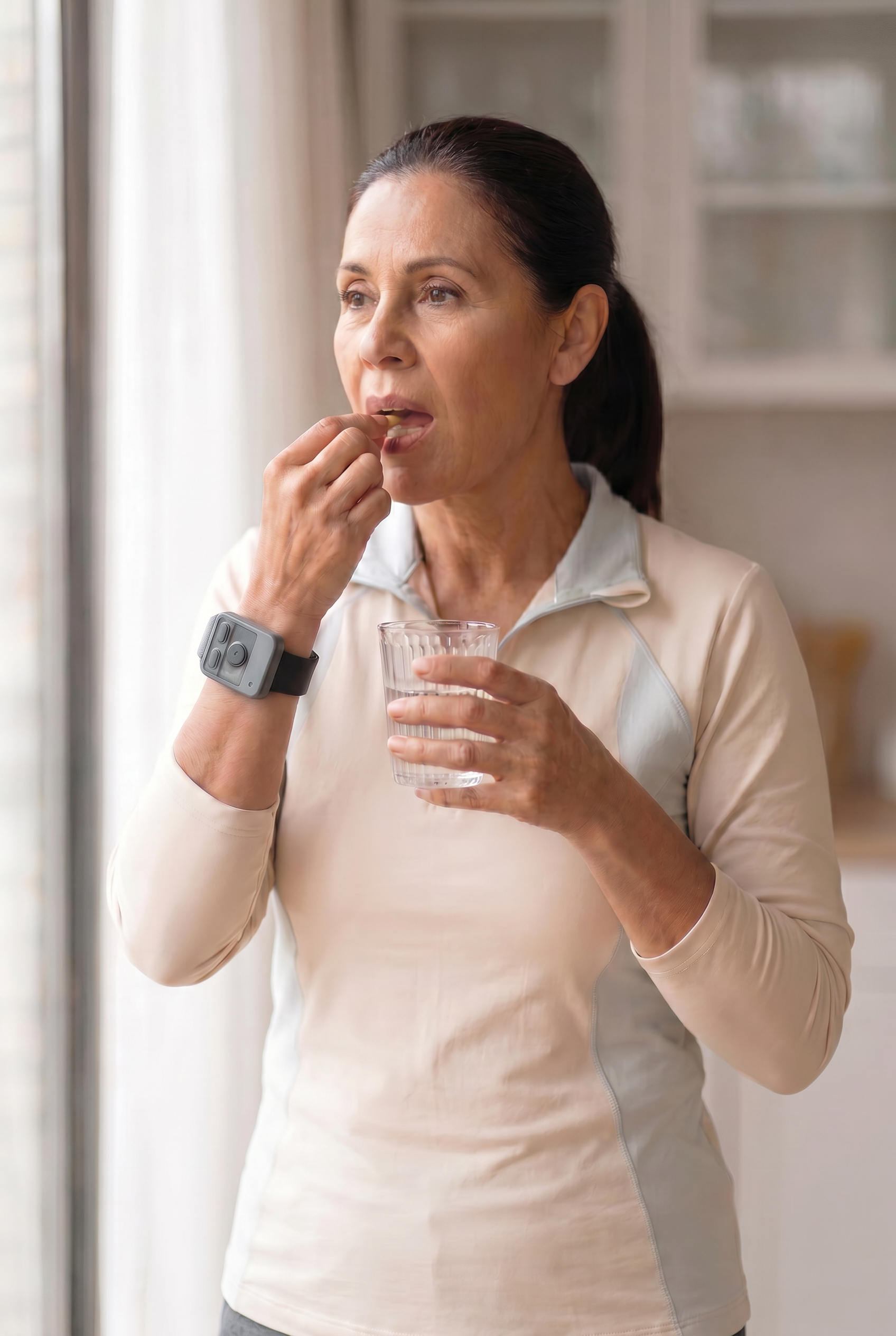 A woman wearing Encora X1 taking medication with a glass of water