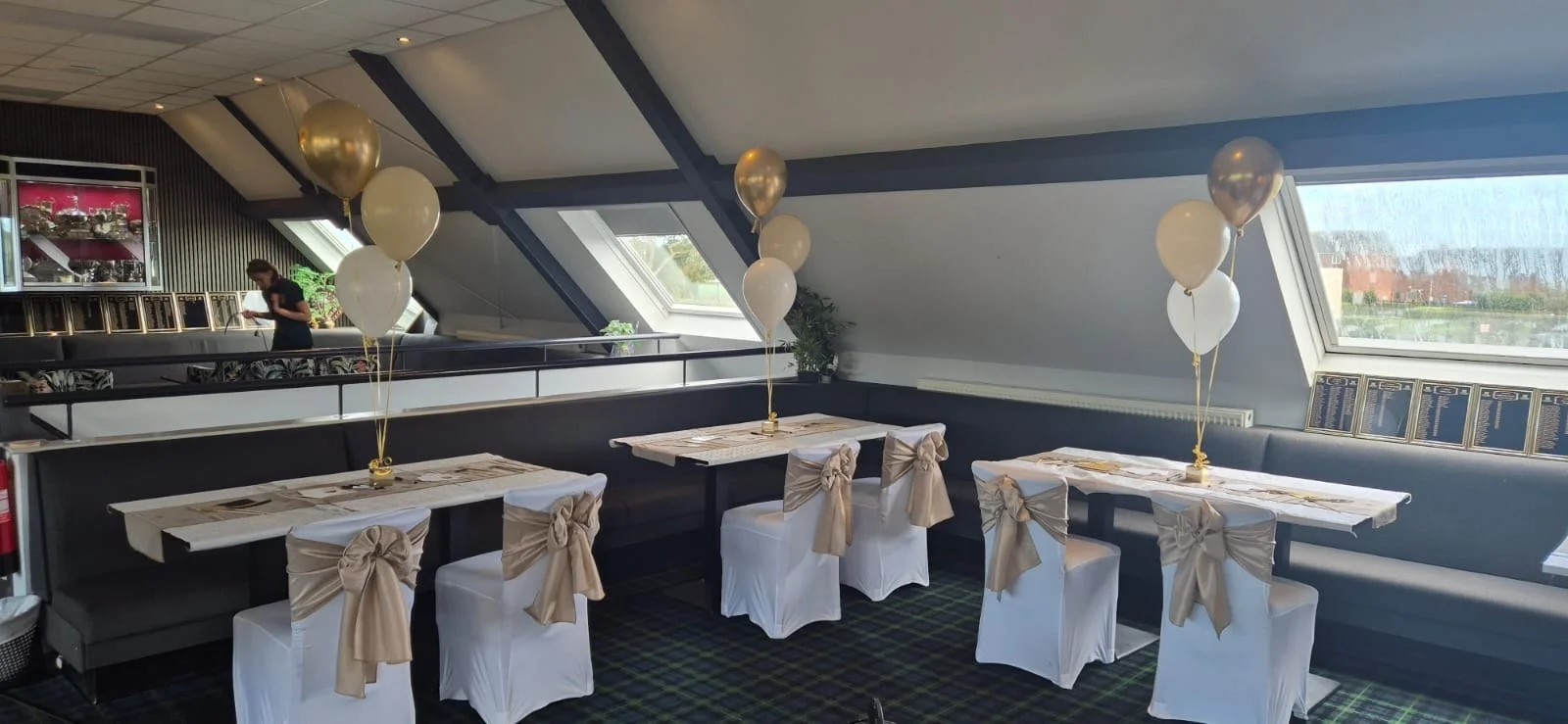 Tables with white chair covers and gold sashes under the sloped ceiling of the 1905 Bar