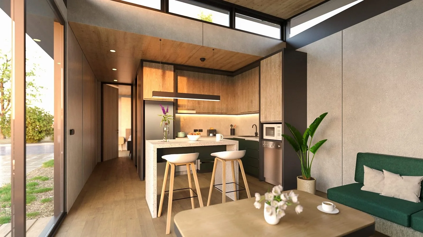Freedom 60 Single kitchen and dining from the glazed wall: timber dining table in front, terrazzo-look island with two stools, green lower cupboards and oak-look overheads, the hallway to the bedroom beyond and a green sofa to the right
