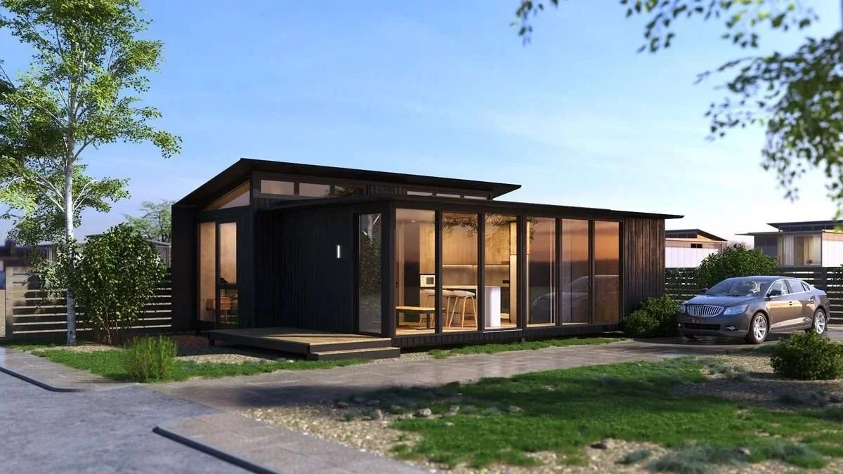 Freedom 60 Double exterior: two dark-clad modules under a raised skillion roof, full-height glazing and a timber deck, trees behind