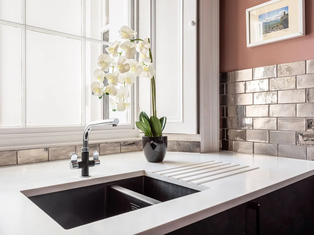 Minerva worktop with grooved drainer beside the kitchen sash window and silver wall tiles