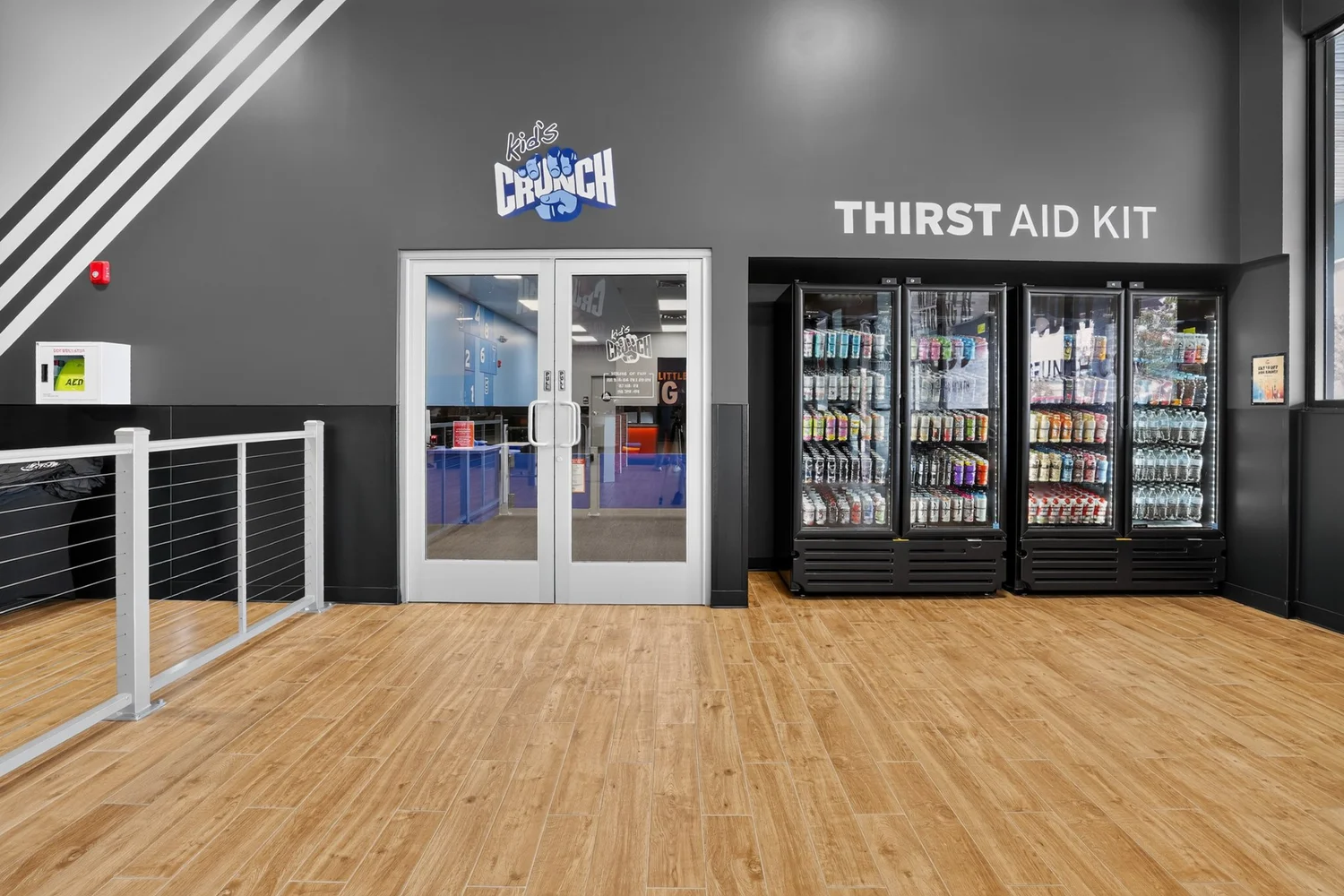 A landing at the top of the stairs, glass doors into a studio beside glass-fronted drinks coolers.