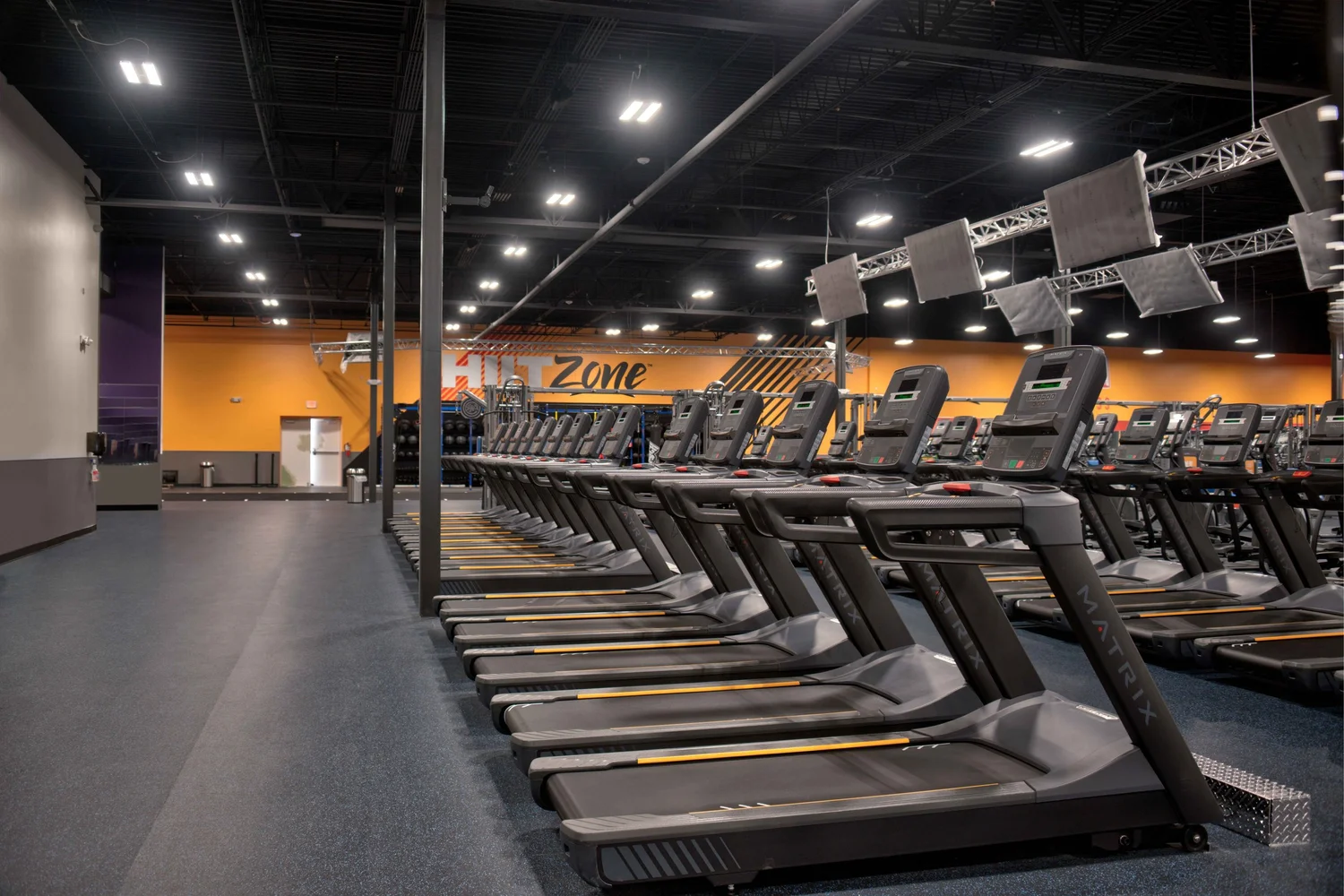 A long row of treadmills running the depth of the club, the HIIT Zone sign on an orange wall beyond.