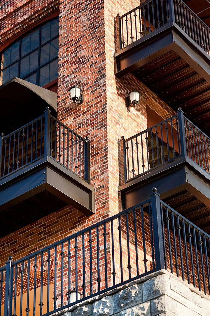 A brick pier with balconies either side, black railings topped with spear finials and two wall lanterns.