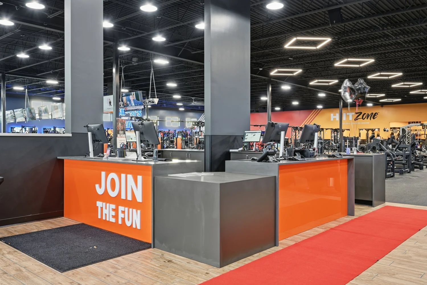 The front desk, an orange and grey counter lettered Join The Fun, a red runner leading into the club.