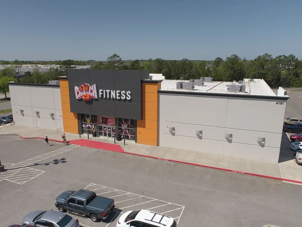 A pale grey box seen from above, its dark sign block flanked by orange piers, a red walkway leading to the doors.