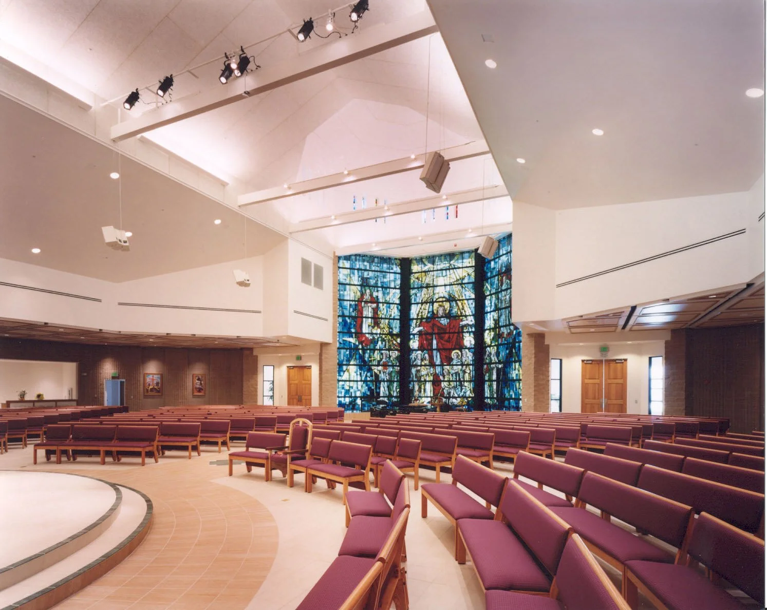 Curved rows of pews and chairs sweeping towards the blue-lit stained glass wall.