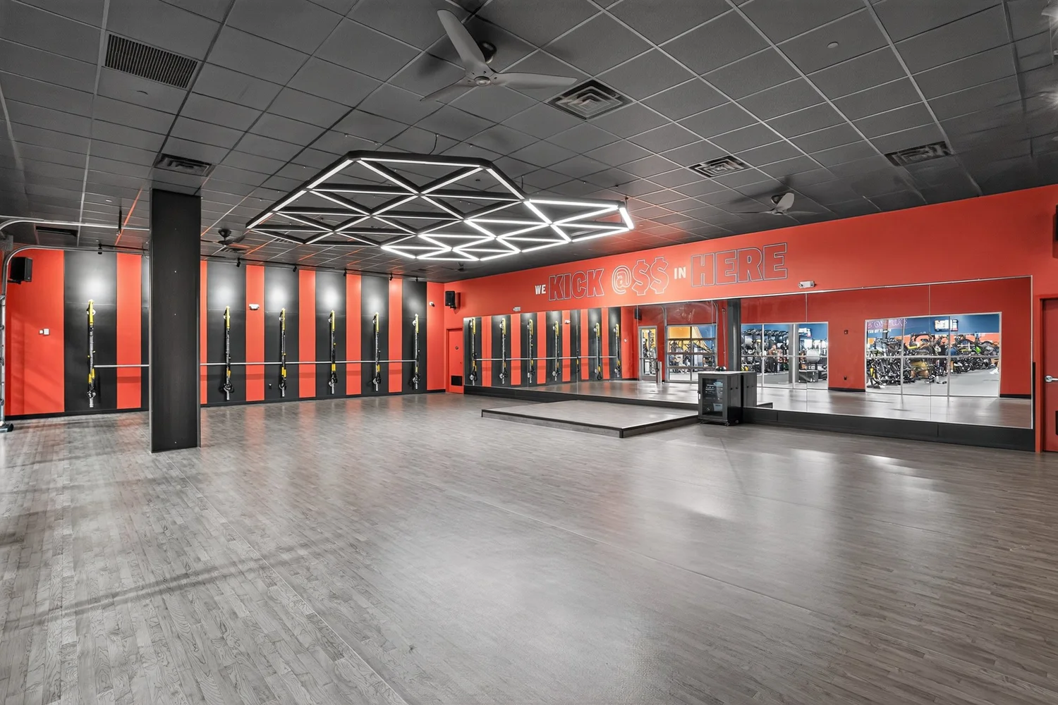 A studio with a mirrored end wall and low stage, TRX straps hanging along a red wall.