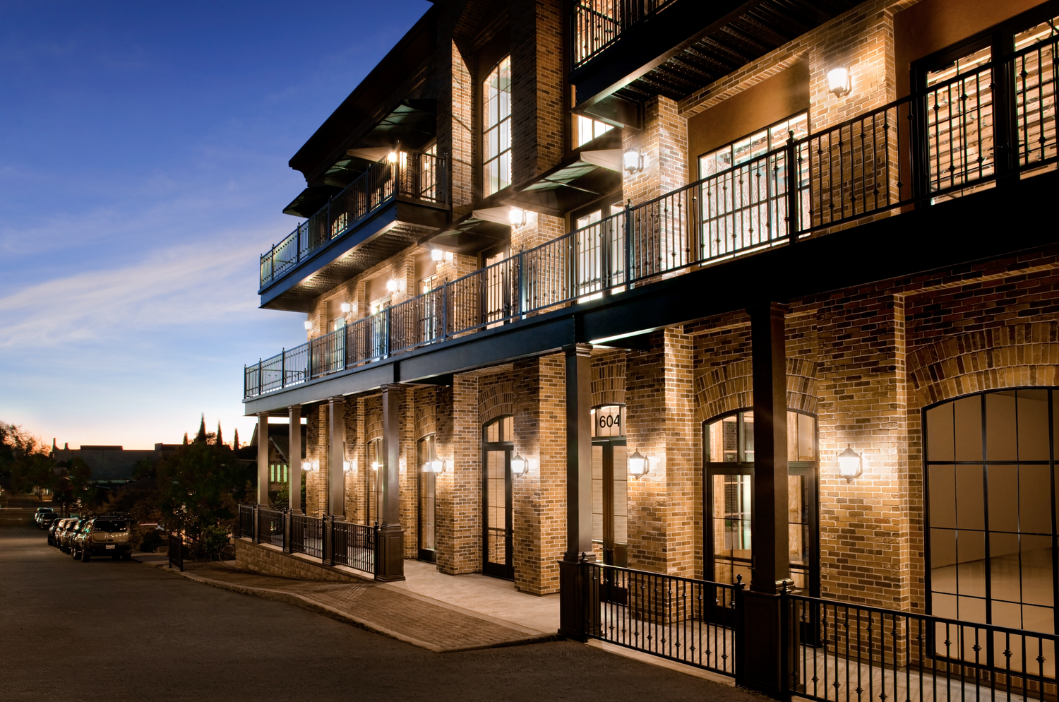 The street front at dusk, three storeys of lit balconies over brick arches and a doorway numbered 604.
