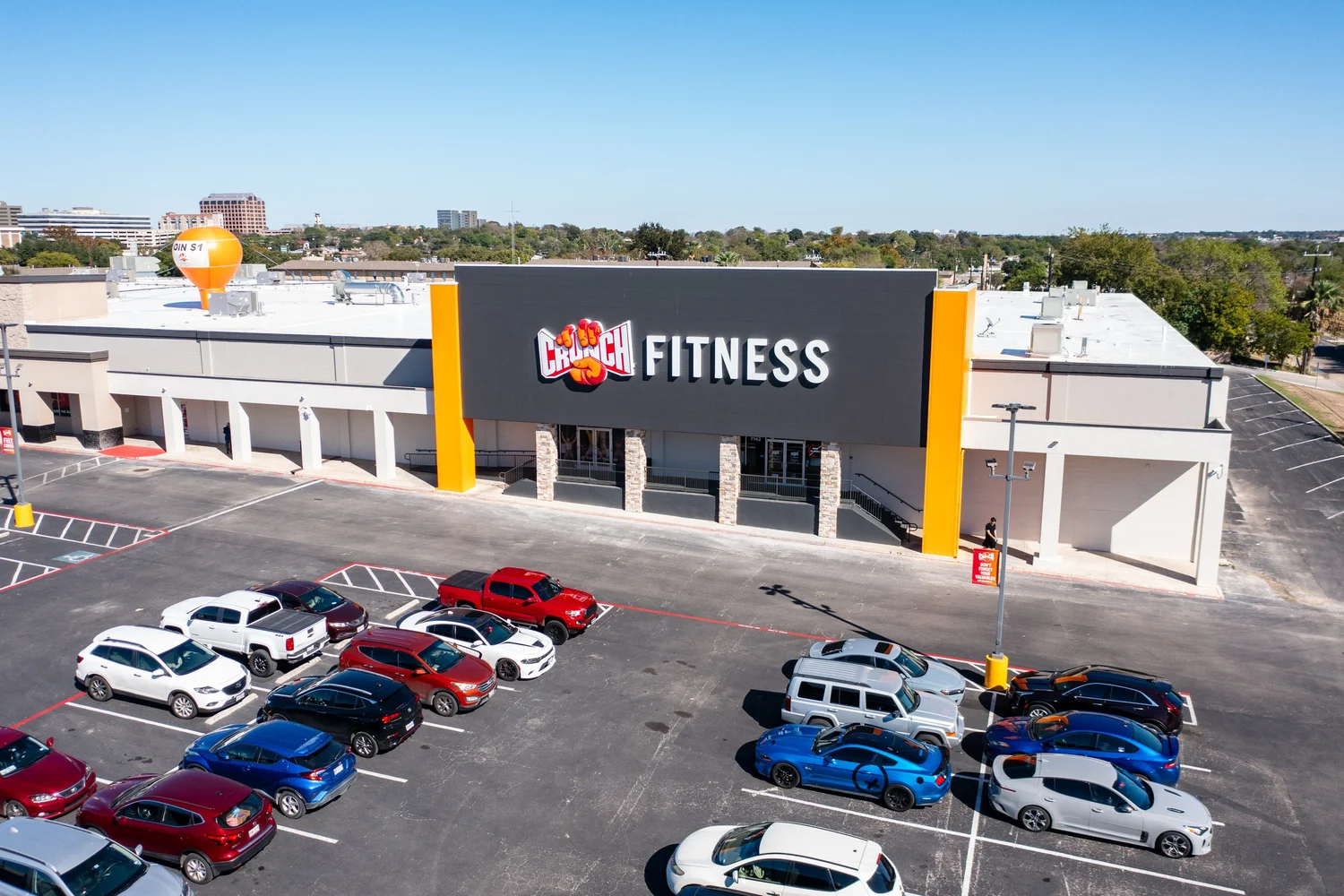 A grey sign block with yellow piers rising above a cream strip centre, a tall orange balloon on the roof.