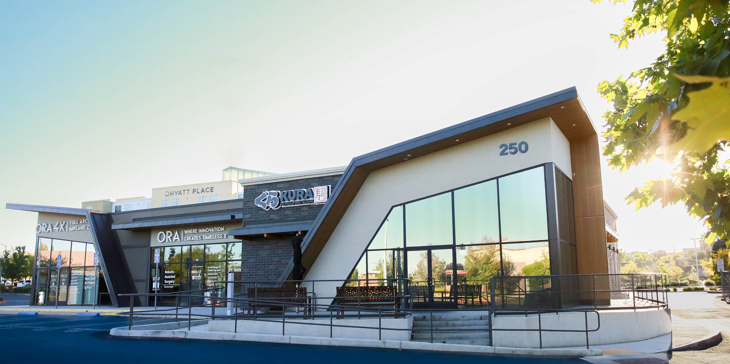 The restaurant on its corner in low sun, its folded white frontage cantilevered over full-height glazing.