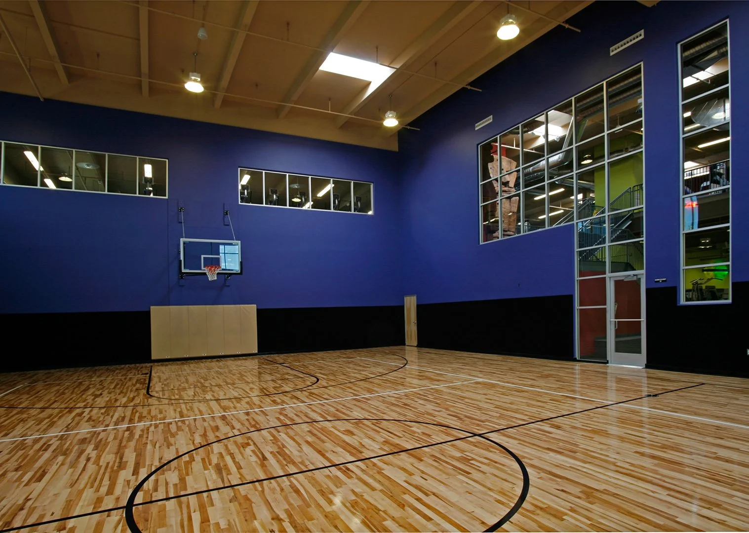 The indoor basketball court, a timber floor marked in black between deep blue walls under clerestory windows.
