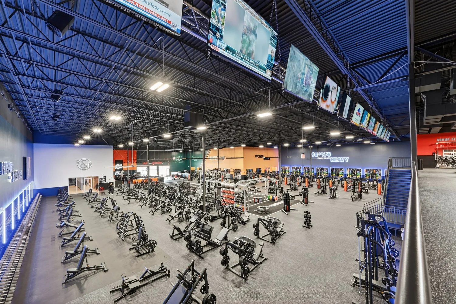 The machine floor down its length, ranks of plate-loaded machines under an exposed blue-painted roof.