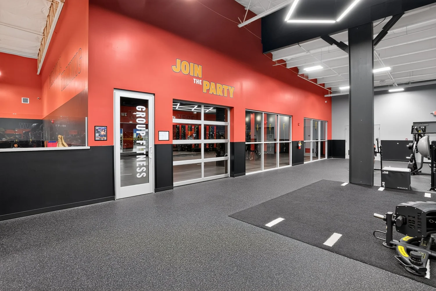 The way into the group fitness studio, glass doors under a red wall lettered Join The Party.