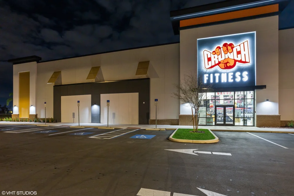 The club at night, its illuminated Crunch Fitness sign glowing on a dark facade above lit entrance doors.