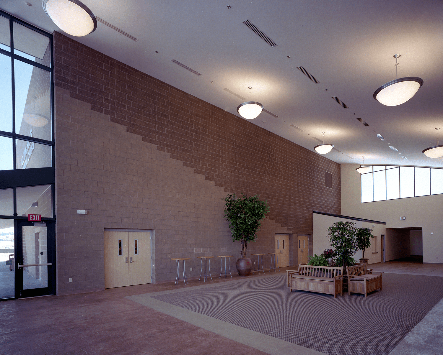 The lobby, a tall brick wall stepping upward beneath a row of bowl pendant lights and a high ceiling.