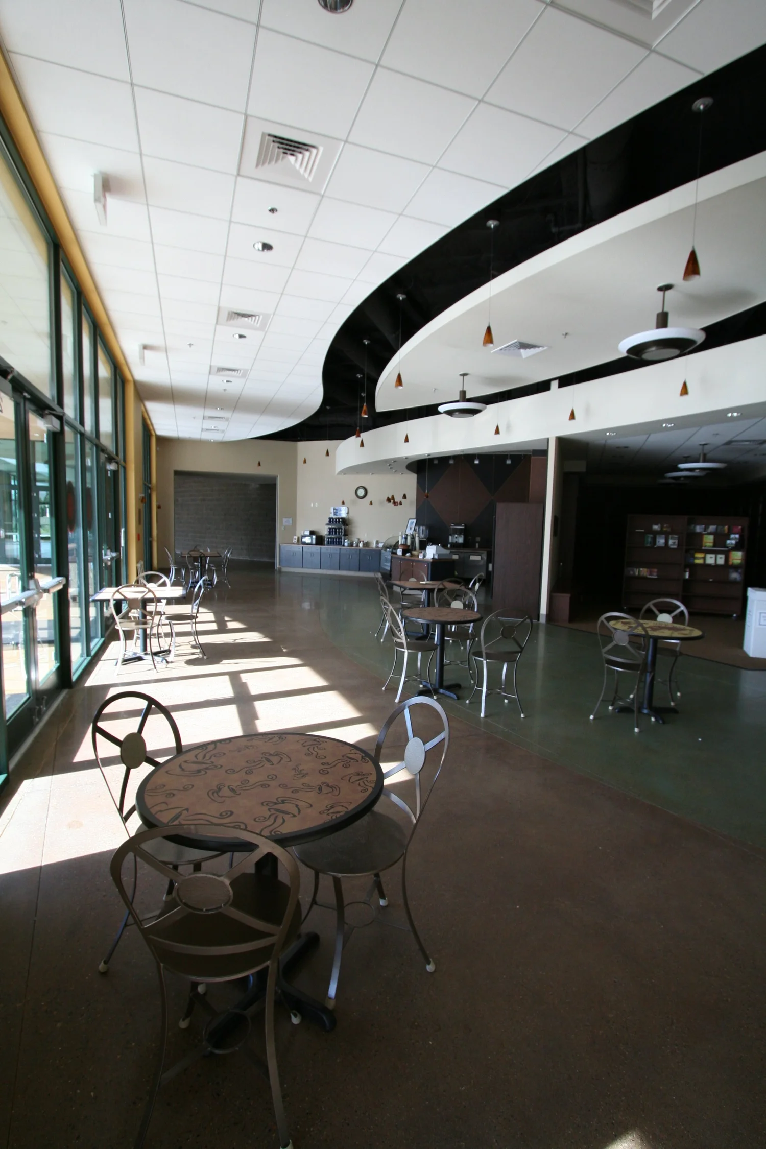 The fellowship area, round bistro tables on polished concrete with sun through the glass wall and the cafe beyond.