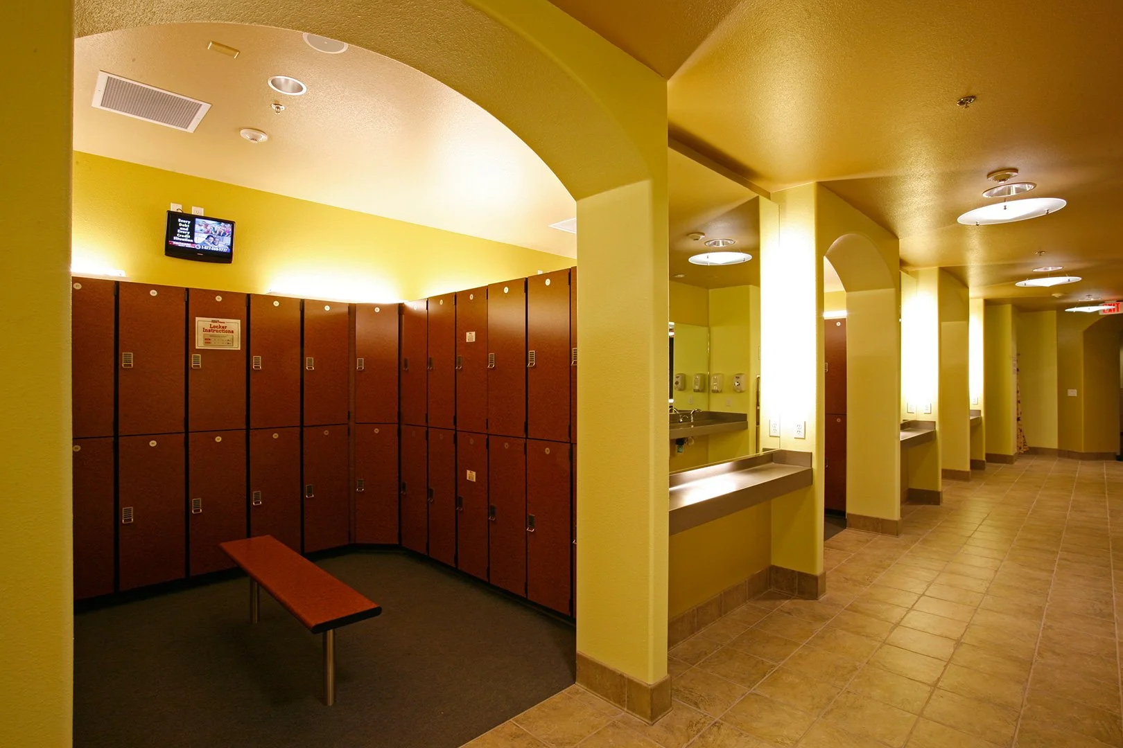 The locker room, dark red lockers in two tiers around a bench under a low barrel vault.