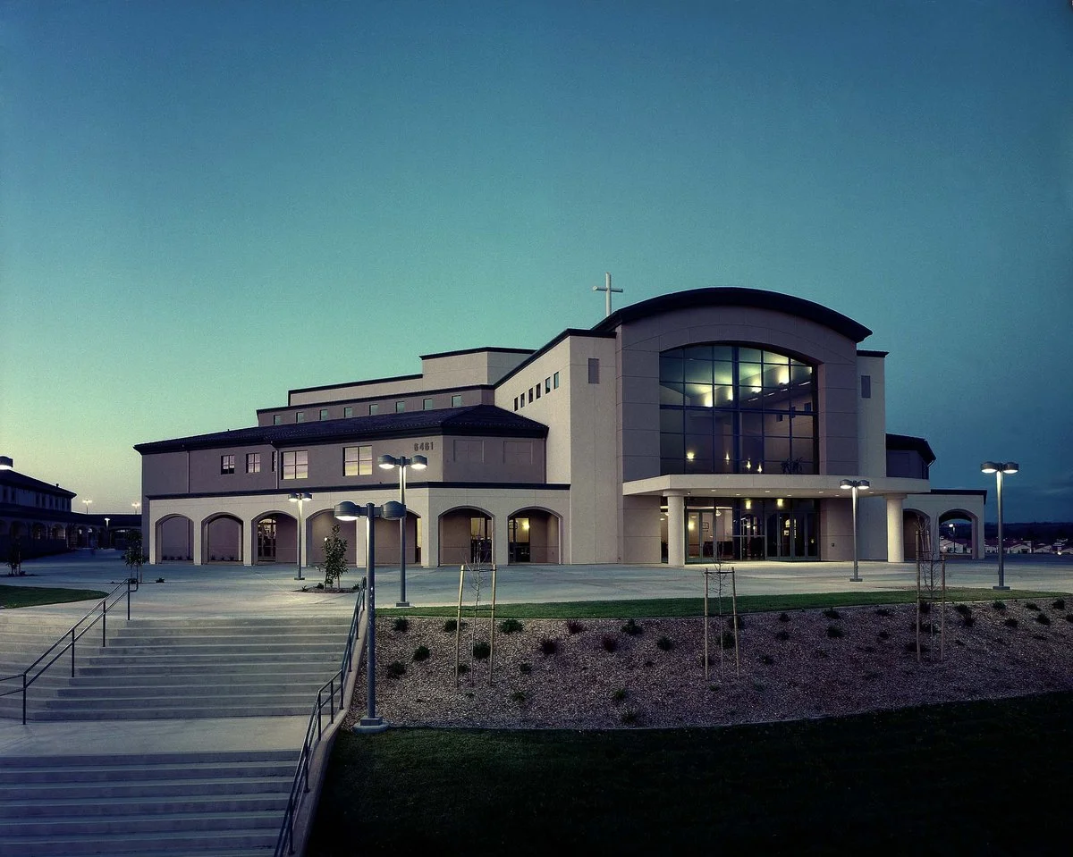 The building at dusk from the side, its arcade lit along the whole length and the entrance window glowing.
