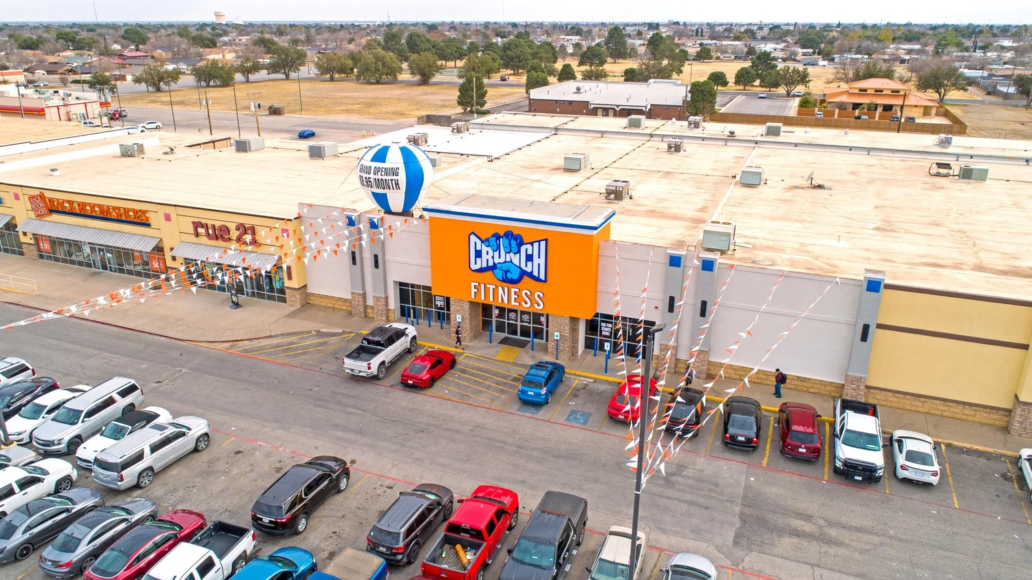 An orange sign block over the entrance of a long strip centre, orange bunting strung across the frontage.