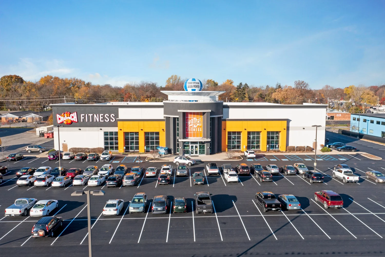 An aerial view of a long white and grey box with yellow bays and a domed entrance tower, its parking lot full.