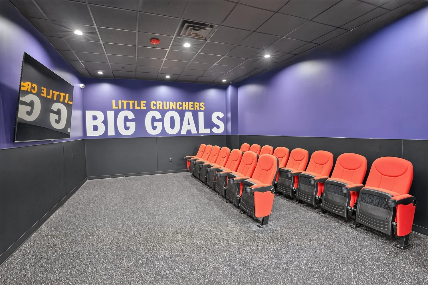 A room for children with purple walls, orange theatre seats under Little Crunchers Big Goals.
