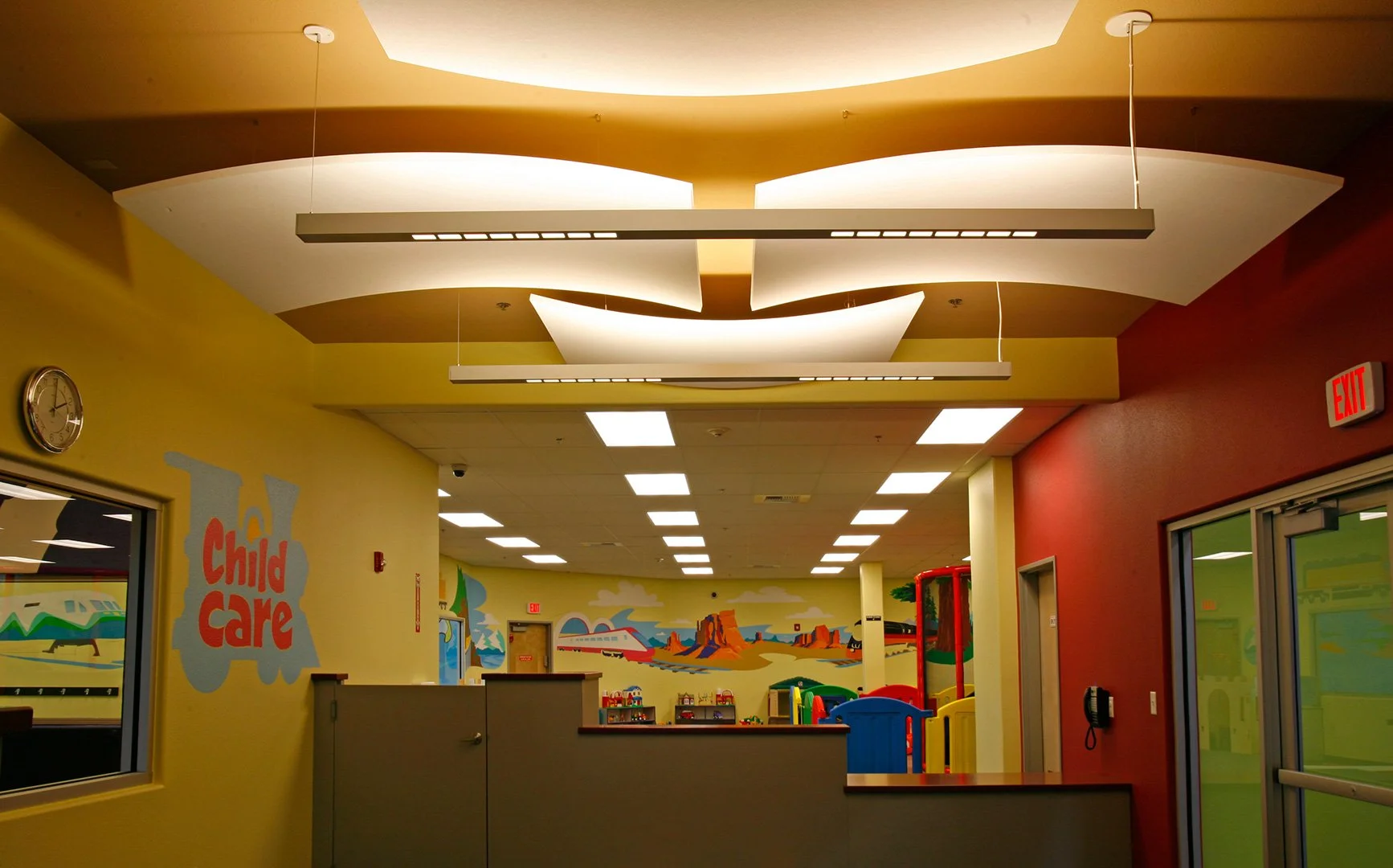 The child care entrance, a counter under a folded ceiling of lit coves beside a viewing window.