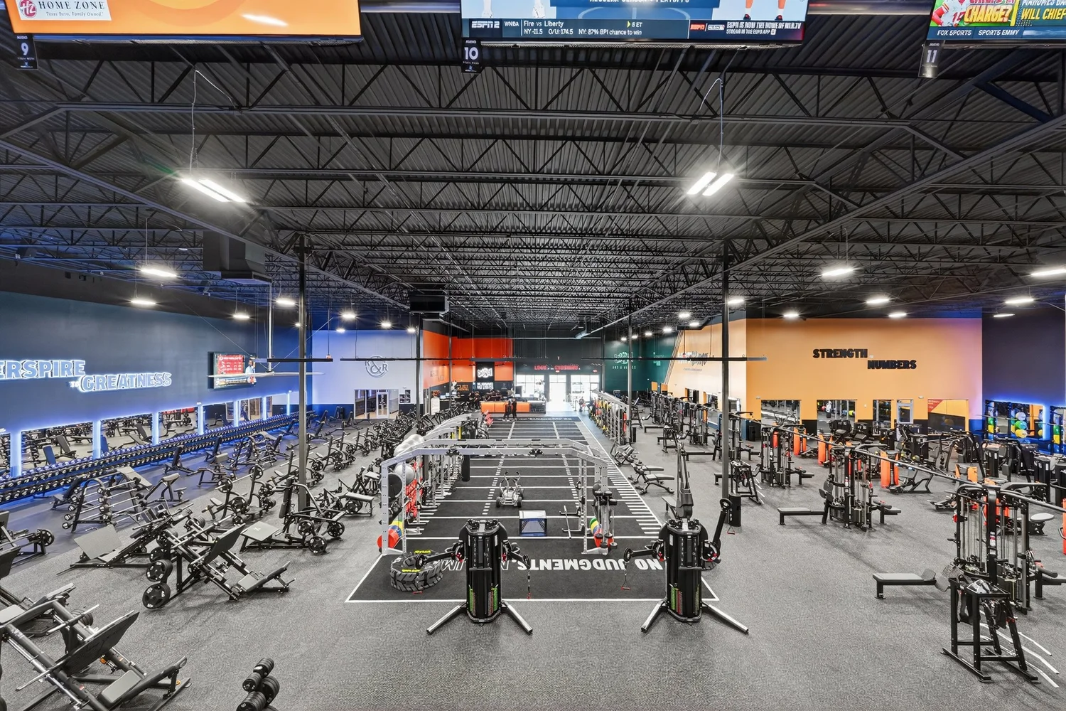 The training floor wide, machines, benches and racks under an exposed steel roof, No Judgments on the floor.