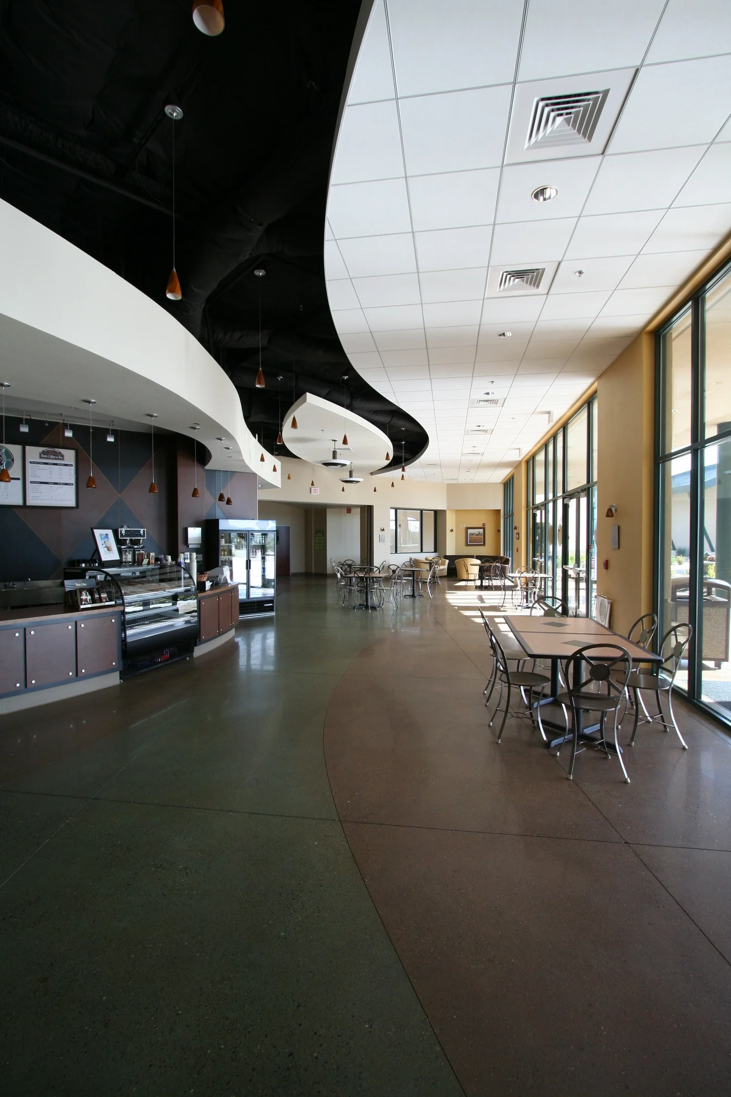The cafe counter and pastry case under a curved white soffit sweeping across an open black ceiling.