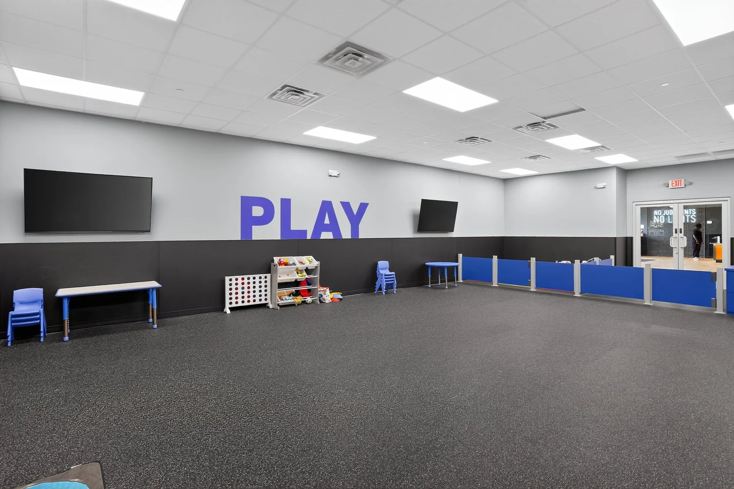 A play room for children, screens on two walls and a blue-panelled barrier lettered Play.