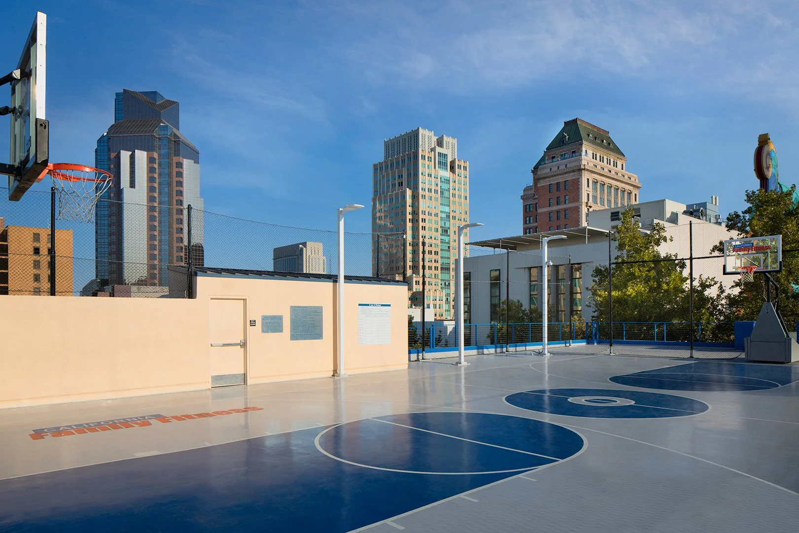 The court from the opposite baseline, the club's name stencilled in orange across the deck, skyline beyond.