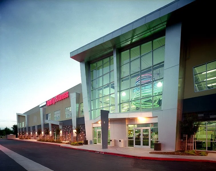 The entrance elevation at dusk, the glazed bay glowing green and white above a canopy over the doors.