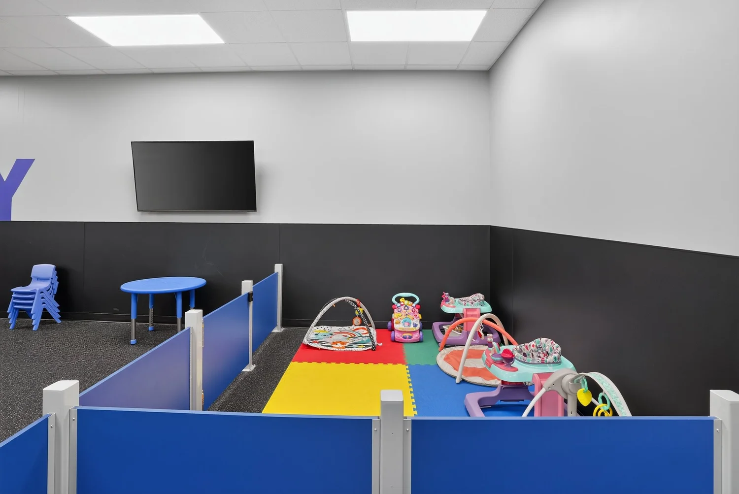 The childcare room, a low blue-panelled enclosure with a soft play mat, bouncers and activity frames.