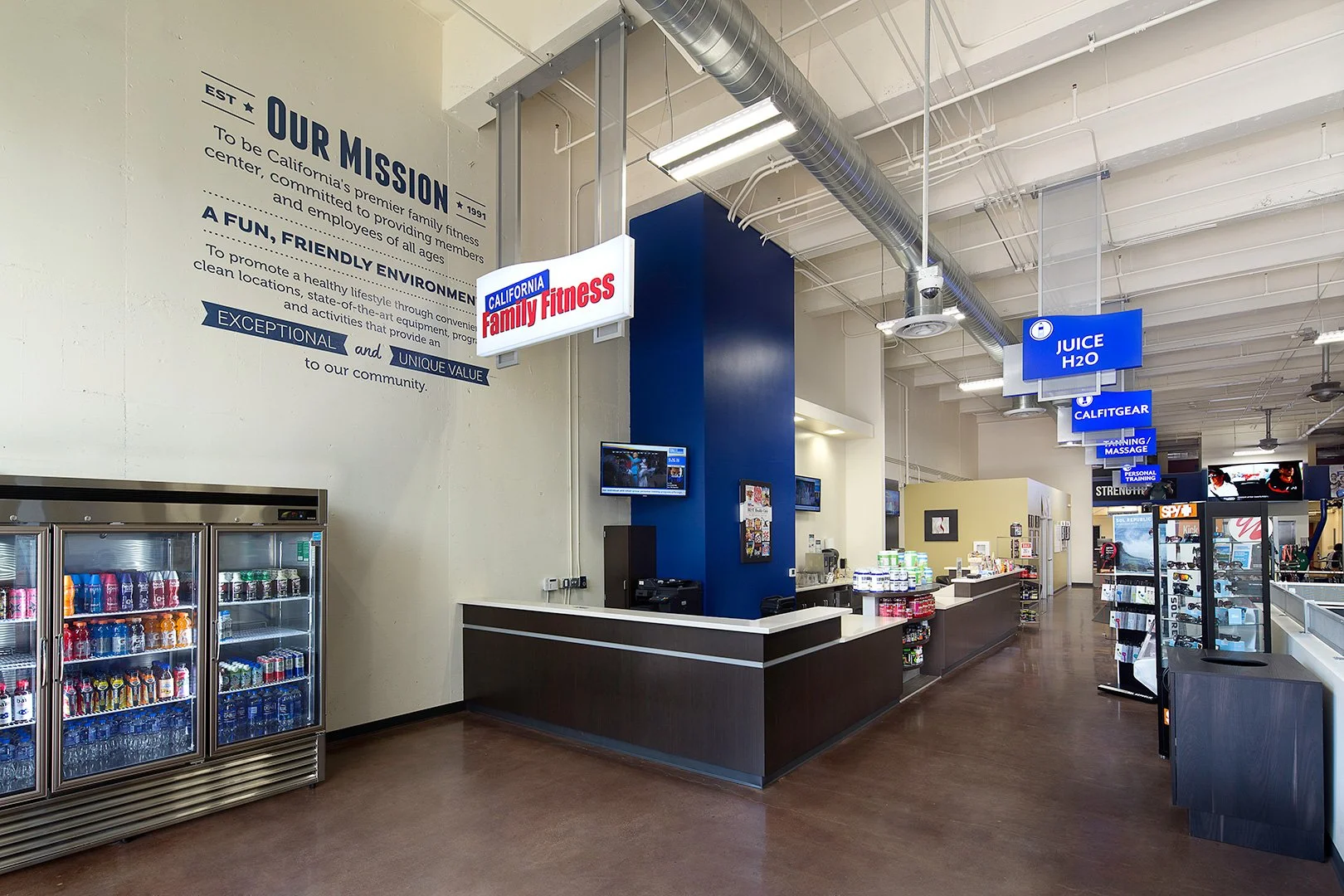 The front counter turning a deep blue column under exposed ductwork, hanging signs running away to the right.