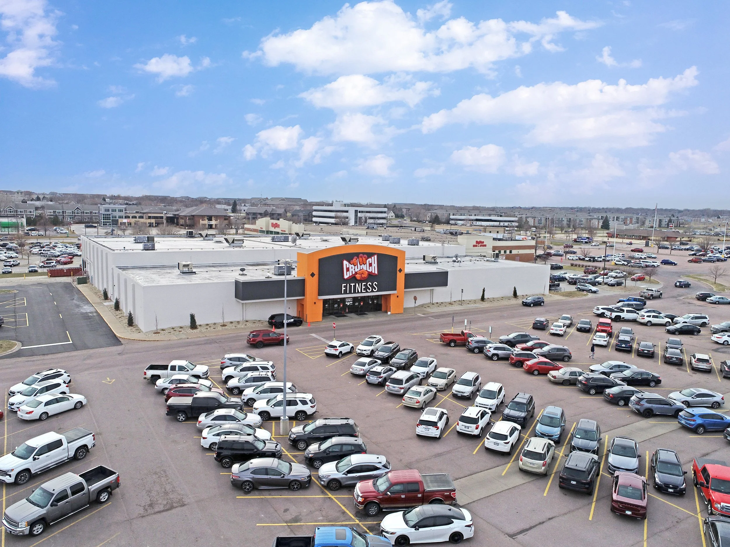 A long white box seen from above, an orange sign panel marking the recessed entrance, a wide lot in front.