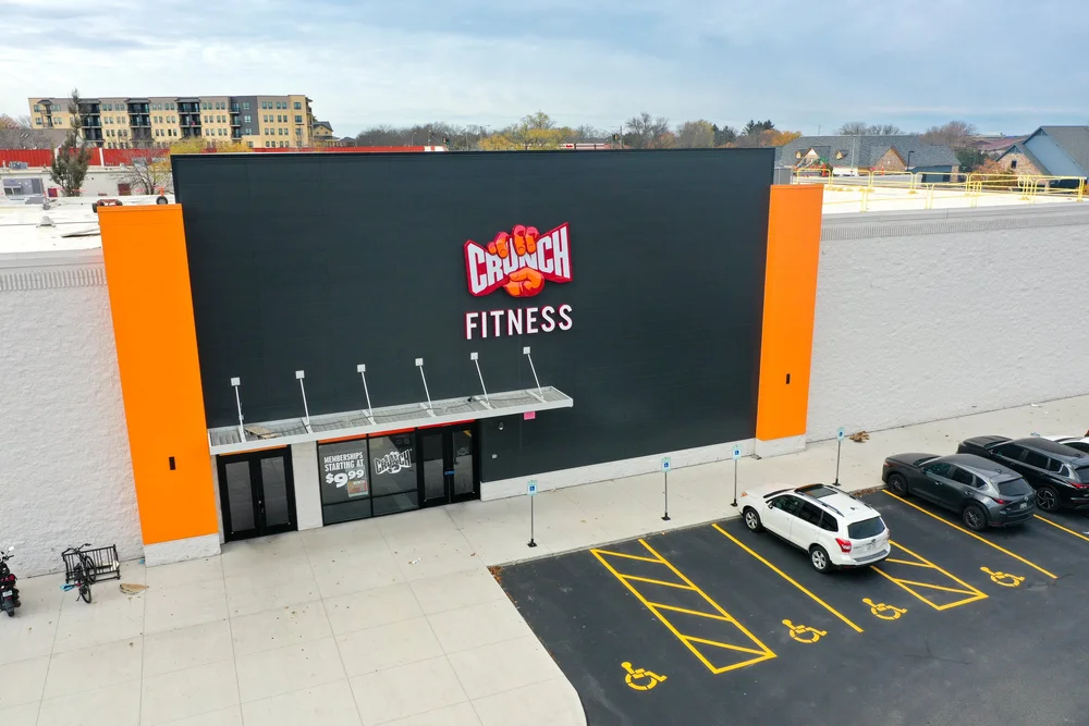A tall black wall between two orange piers, with a slim canopy over the glass entrance doors below.