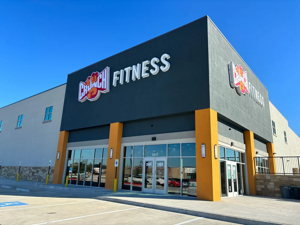 A corner entrance in deep navy with orange piers, an oversized Crunch Fitness sign on both faces.